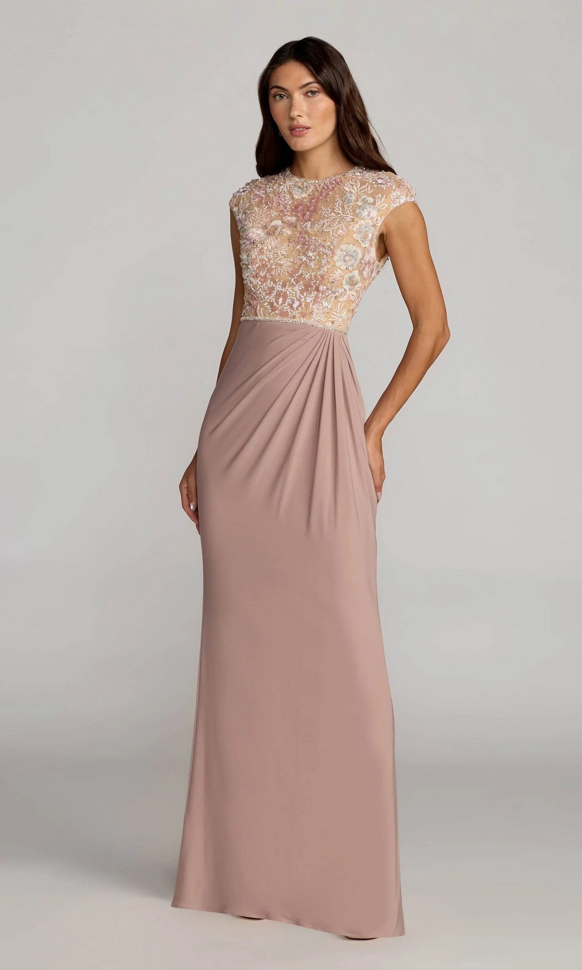 A woman wearing the Mac Duggal 21324 long formal dress in taupe multi, featuring a floor-length design with a fitted, embroidered bodice and cap sleeves, stands against a plain light background.